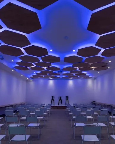 Auditorio con techo de paneles hexagonales iluminados y filas de sillas, en Palermo, Buenos Aires