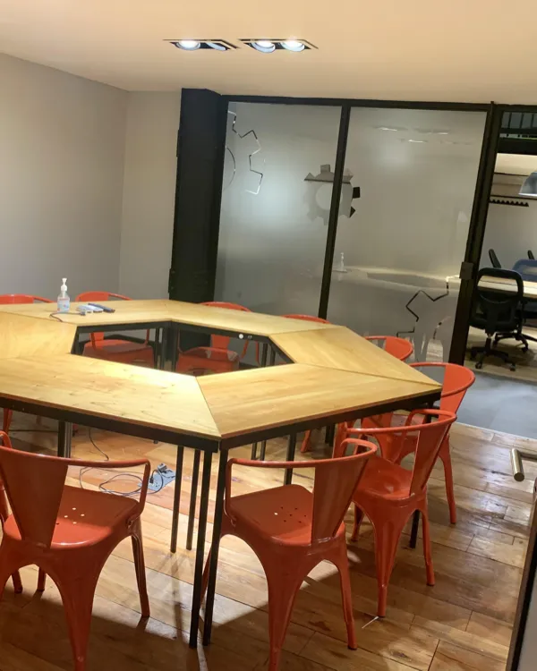 Sala de reuniones con mesa hexagonal de madera y sillas naranjas, en San Nicolás, Buenos Aires
